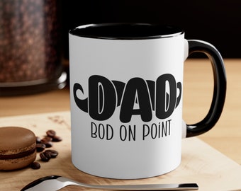 May include: White ceramic coffee mug with a black rim and handle. The mug has a black and white graphic of a mustache with the word "DAD" and the text "BOD ON POINT" below.