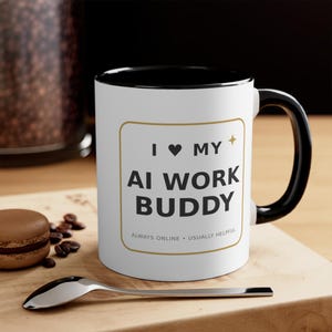 May include: A white ceramic mug with a black handle and interior rim. The front features a gold-bordered square containing the black text I heart MY AI WORK BUDDY and the smaller text ALWAYS ONLINE • USUALLY HELPFUL with a small gold star icon.