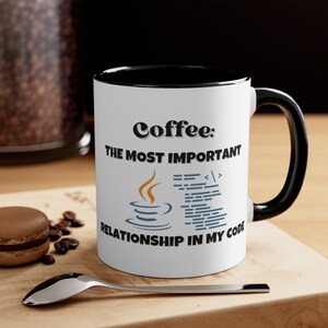 May include: White coffee mug with a black rim and handle. The mug has a black graphic of a coffee cup with steam and code on it. The text on the mug reads "Coffee: The Most Important Relationship In My Code."