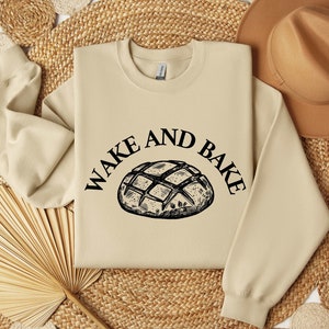 May include: A tan sweatshirt with the text "Wake and Bake" and a black and white illustration of a loaf of bread.