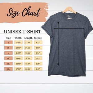 Pu&ograve; includere: Una maglietta unisex grigia su una gruccia di legno. L'immagine include una tabella delle taglie con misure in pollici per larghezza, lunghezza e lunghezza manica per le taglie S-3XL. Sono visibili anche le scritte "Size Chart" e "UNISEX T-SHIRT".