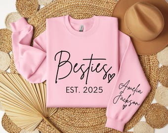 May include: Pink sweatshirt with the text "Besties Est. 2025" and the name "Amelia Jackson" on the sleeve.