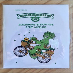 May include: A white flyer with the text "PRESENTED BY MUNCHINMONSTER" and an illustration of a green monster riding a bicycle with a basket of vegetables and a sunflower. The flyer is in a clear plastic sleeve.