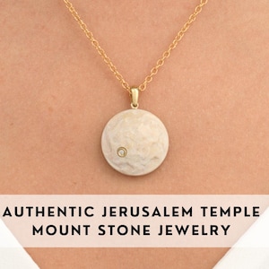 Może przedstawiać: Złoty łańcuszek z okrągłym wisiorem wykonanym z białego kamienia z małym diamentowym akcentem. Wisiorek ma fakturowaną powierzchnię. AUTENTYCZNA BIŻUTERIA Z KAMIENIA Z GÓRY ŚWIĄTYNI JEROZOLIMSKIEJ