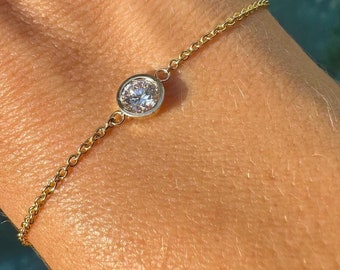 May include: A delicate gold chain bracelet with a single, round, clear gemstone.
