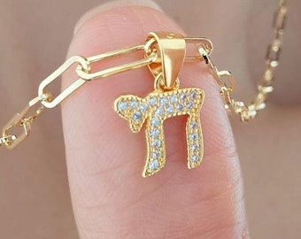 May include: A gold chain necklace with a small pendant featuring the Hebrew letter 'Chai' set with clear cubic zirconia stones.