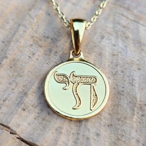 A gold-colored pendant necklace with a circular medallion featuring a symbol or text.