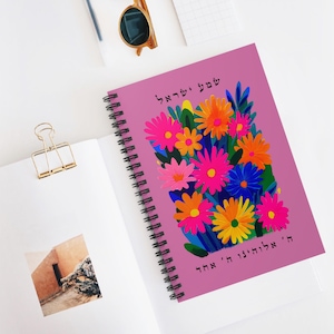 Puede incluir: Un cuaderno de espiral rosa con una cubierta con un diseño floral colorido. Las flores son en tonos de rosa, naranja, amarillo y azul. El cuaderno está abierto, revelando páginas en blanco, junto a otro cuaderno blanco.