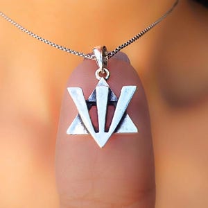 A silver pendant with a triangular symbol is hanging from a chain around a person's neck.