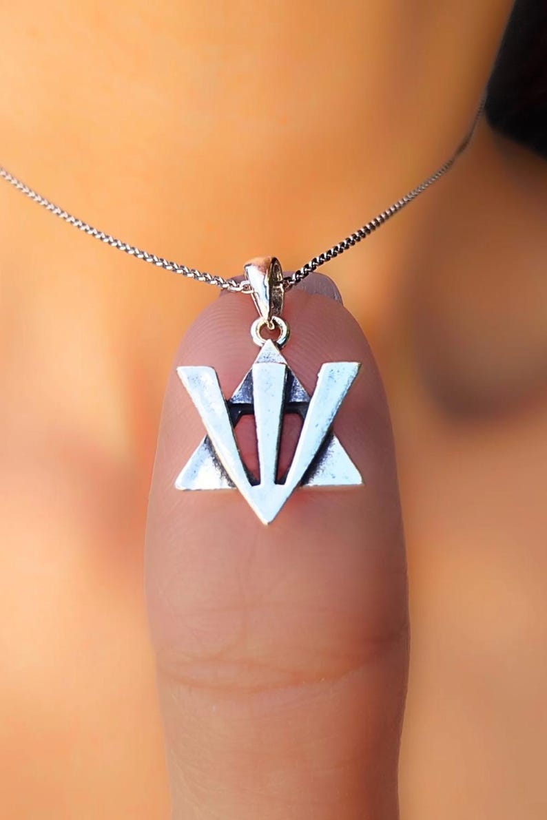 A silver pendant with a triangular symbol is hanging from a chain around a person's neck.