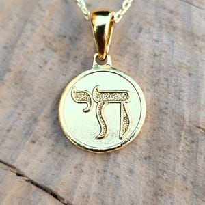 A gold-colored pendant necklace with a circular medallion featuring an embossed symbol.