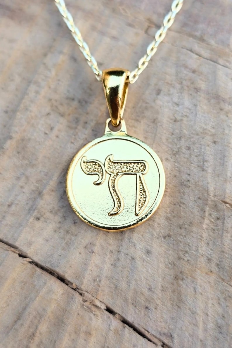 A gold-colored pendant necklace with a circular medallion featuring an embossed symbol.