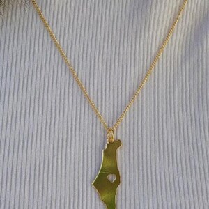 A gold-colored necklace with a pendant in the shape of a green leaf.