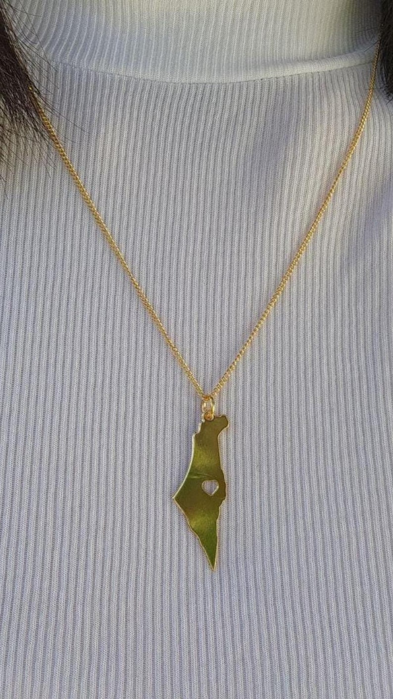 A gold-colored necklace with a pendant in the shape of a green leaf.
