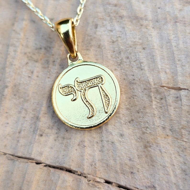 A gold-colored pendant with a circular design on it, resting on a wooden surface.