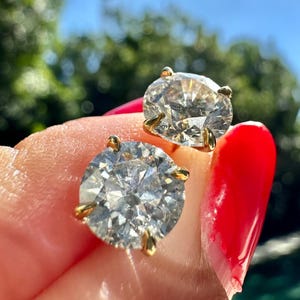 Pode incluir: Um par de brincos de pressão de ouro com grandes pedras preciosas redondas, transparentes e facetadas.