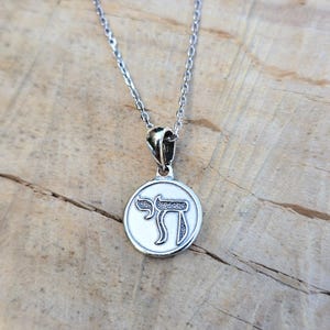 A silver necklace with a circular pendant featuring a symbol or design.