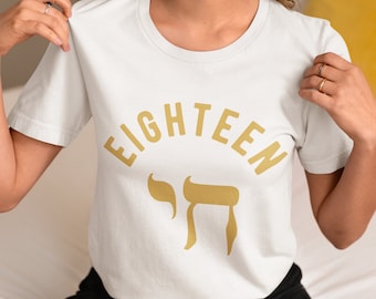 May include: White t-shirt with the word "EIGHTEEN" in gold lettering and a gold Hebrew letter "Chai" symbol.