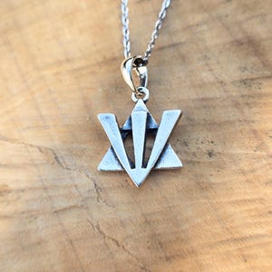 A silver-colored pendant necklace with a triangular symbol on it, resting on a wooden surface.