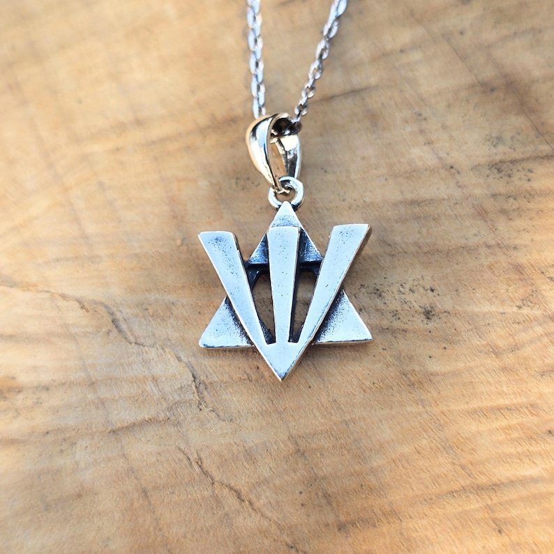 A silver-colored pendant necklace with a triangular symbol on it, resting on a wooden surface.