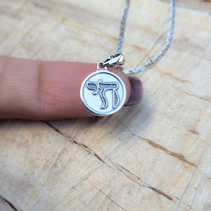 A silver pendant necklace with a circular charm featuring an image of a hand holding a book.
