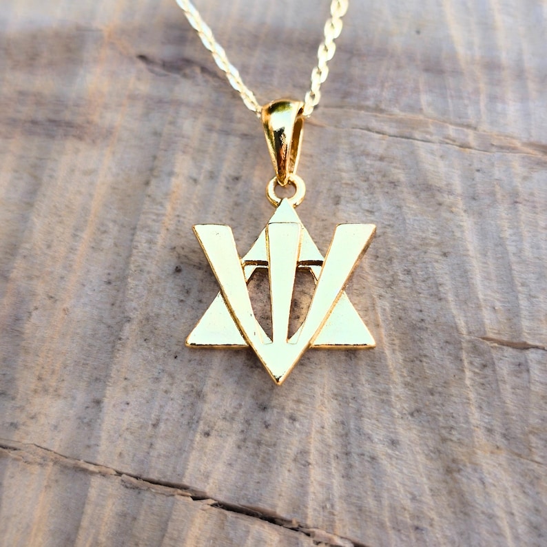 A gold-colored pendant necklace with a triangular symbol on a wooden surface.