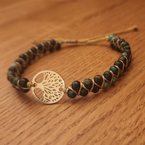 Puede incluir: Un brazalete de oro con un dije de árbol de la vida, cuentas turquesa y marrones y un cordón de color beige.