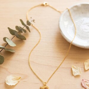 May include: A gold-colored necklace featuring a delicate chain and a pendant shaped like the Hebrew letter Chai. The pendant is suspended from a thin, polished metal chain that includes a small circular clasp mechanism at the back of the necklace.