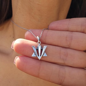 A person is holding a silver pendant with a triangular design on a chain around their neck.
