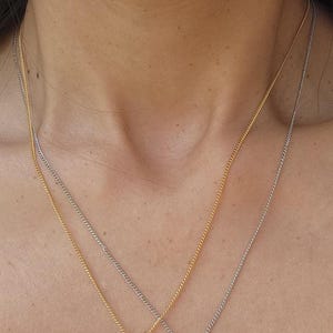 A close-up of a person's neck with two pendant necklaces, each with a ribbon charm.
