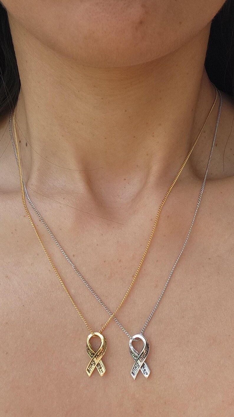 A close-up of a person's neck with two pendant necklaces, each with a ribbon charm.