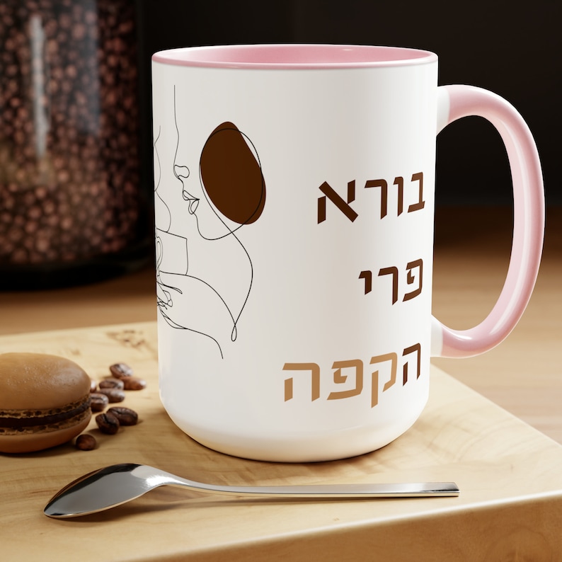 May include: White ceramic coffee mug with a pink rim and handle. The mug features a line drawing of a woman drinking coffee with the text "Good morning" in Hebrew.