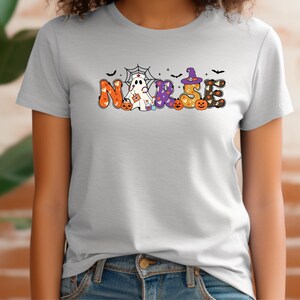 May include: A light gray t-shirt with a Halloween-themed design that says "NURSE" in colorful letters with ghosts, pumpkins, and bats.