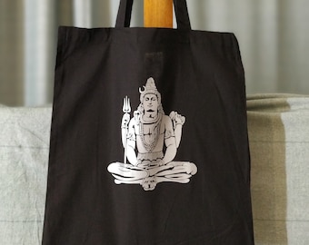 May include: Black tote bag with a white image of a Hindu deity, Shiva, sitting in a meditative pose.