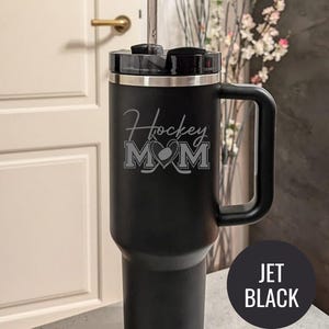 Engraved Hockey Mom tumbler with hockey stick and heart design; stainless steel insulated travel cup with handle; personalized drinkware for sports moms; custom cup for hockey games, practices, or gifts; durable large-capacity tumbler perfect for birthdays, holidays, and hockey season celebrations; stylish engraved design for everyday use.