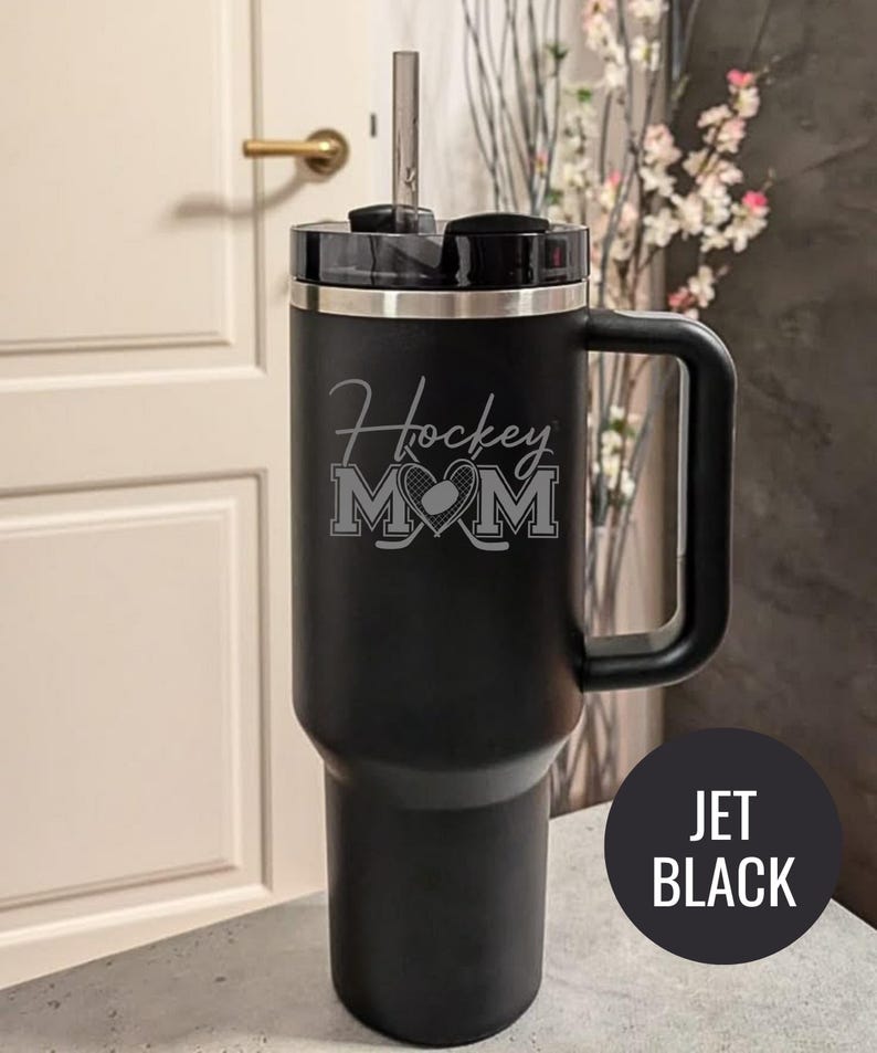 Engraved Hockey Mom tumbler with hockey stick and heart design; stainless steel insulated travel cup with handle; personalized drinkware for sports moms; custom cup for hockey games, practices, or gifts; durable large-capacity tumbler perfect for birthdays, holidays, and hockey season celebrations; stylish engraved design for everyday use.