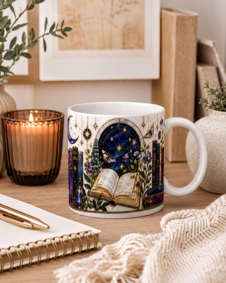 A white mug with a colorful illustration of a book, flowers, and a starry night sky, placed on a wooden surface next to a notebook, a candle, and some books.