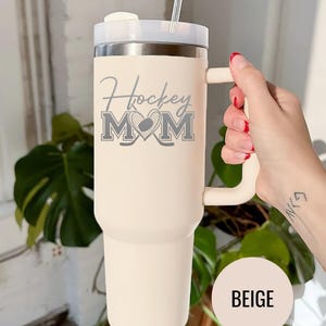 Engraved Hockey Mom tumbler with hockey stick and heart design; stainless steel insulated travel cup with handle; personalized drinkware for sports moms; custom cup for hockey games, practices, or gifts; durable large-capacity tumbler perfect for birthdays, holidays, and hockey season celebrations; stylish engraved design for everyday use.