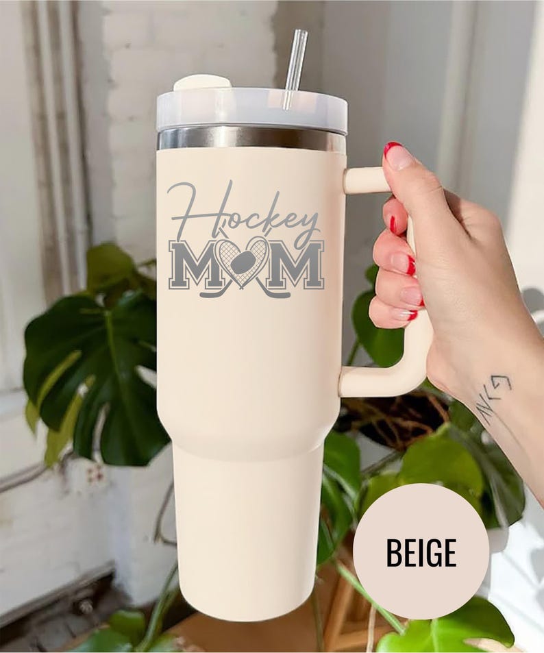 Engraved Hockey Mom tumbler with hockey stick and heart design; stainless steel insulated travel cup with handle; personalized drinkware for sports moms; custom cup for hockey games, practices, or gifts; durable large-capacity tumbler perfect for birthdays, holidays, and hockey season celebrations; stylish engraved design for everyday use.