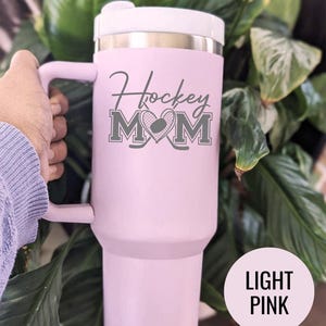 Engraved Hockey Mom tumbler with hockey stick and heart design; stainless steel insulated travel cup with handle; personalized drinkware for sports moms; custom cup for hockey games, practices, or gifts; durable large-capacity tumbler perfect for birthdays, holidays, and hockey season celebrations; stylish engraved design for everyday use.