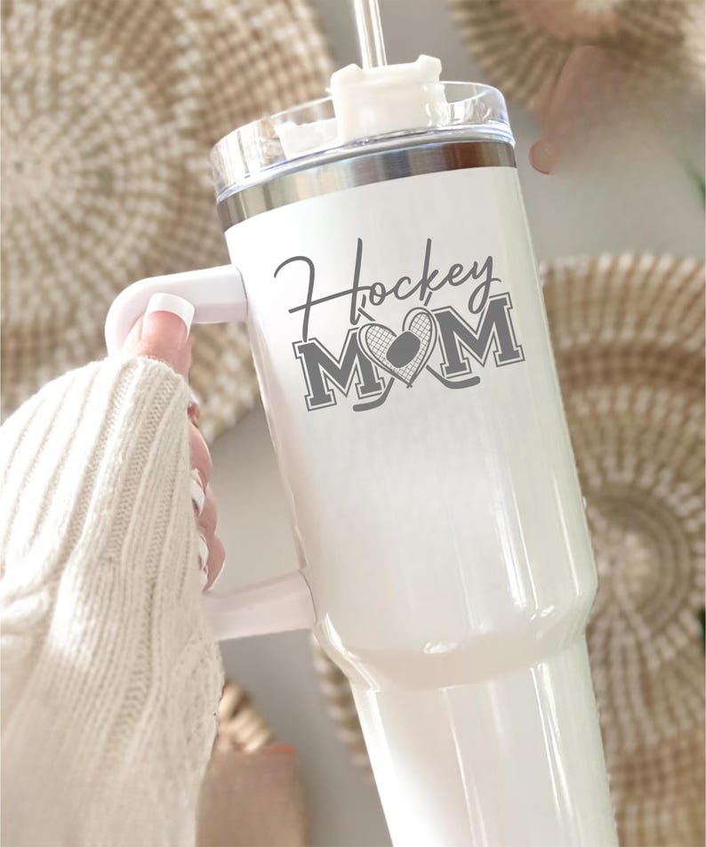 Engraved Hockey Mom tumbler with hockey stick and heart design; stainless steel insulated travel cup with handle; personalized drinkware for sports moms; custom cup for hockey games, practices, or gifts; durable large-capacity tumbler perfect for birthdays, holidays, and hockey season celebrations; stylish engraved design for everyday use.