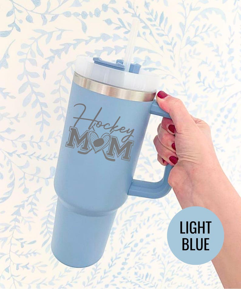 Engraved Hockey Mom tumbler with hockey stick and heart design; stainless steel insulated travel cup with handle; personalized drinkware for sports moms; custom cup for hockey games, practices, or gifts; durable large-capacity tumbler perfect for birthdays, holidays, and hockey season celebrations; stylish engraved design for everyday use.