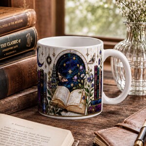 a mug with a starry night sky design, a book, a pen, and a vase of flowers on a wooden surface.