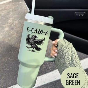 A stainless steel insulated tumbler featuring a detailed black raven illustration with wings spread, paired with the phrase "F-Caw-F" in playful script; the design blends gothic and humorous elements, creating a unique travel cup for bird enthusiasts, crow lovers, or fans of dark sarcastic quotes; shown on tumblers in various matte finishes, each with a handle and straw for practical everyday use.