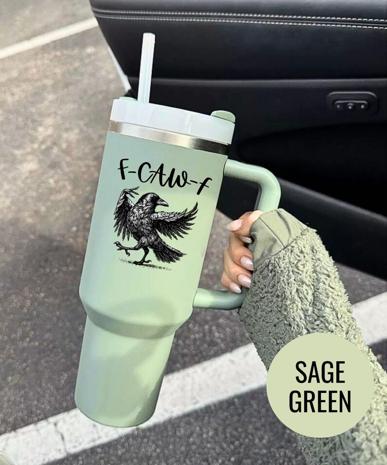 A stainless steel insulated tumbler featuring a detailed black raven illustration with wings spread, paired with the phrase "F-Caw-F" in playful script; the design blends gothic and humorous elements, creating a unique travel cup for bird enthusiasts, crow lovers, or fans of dark sarcastic quotes; shown on tumblers in various matte finishes, each with a handle and straw for practical everyday use.