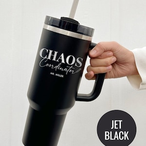May include: A black tumbler with a handle and a lid, featuring the text "CHAOS Coordinator" in silver script. The tumbler includes a straw and the name "MR. MILLER" below the main text. A black circle with "JET BLACK" is in the lower right.