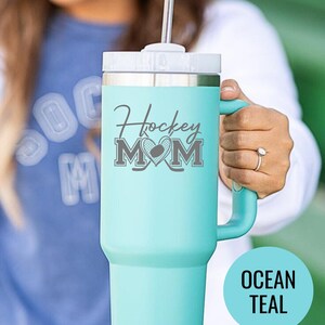 Engraved Hockey Mom tumbler with hockey stick and heart design; stainless steel insulated travel cup with handle; personalized drinkware for sports moms; custom cup for hockey games, practices, or gifts; durable large-capacity tumbler perfect for birthdays, holidays, and hockey season celebrations; stylish engraved design for everyday use.