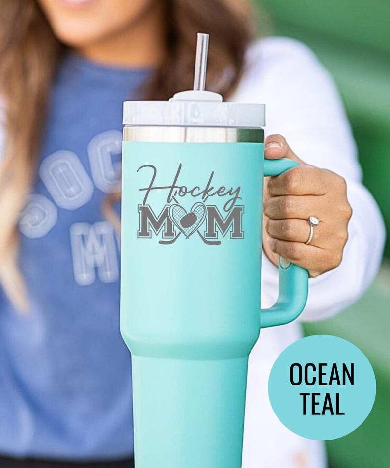 Engraved Hockey Mom tumbler with hockey stick and heart design; stainless steel insulated travel cup with handle; personalized drinkware for sports moms; custom cup for hockey games, practices, or gifts; durable large-capacity tumbler perfect for birthdays, holidays, and hockey season celebrations; stylish engraved design for everyday use.