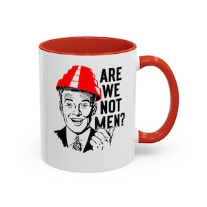 May include: A white ceramic mug with a bright red interior and handle. The front features a black and white illustration of a smiling person wearing a red tiered hat, accompanied by the bold black text that reads: ARE WE NOT MEN?