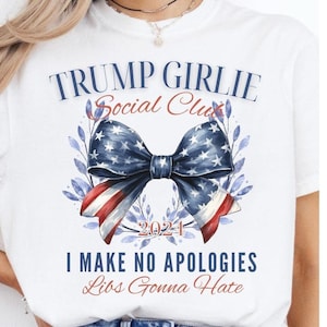 Puede incluir: Camiseta blanca con el texto "TRUMP GIRLIE Social Club" en azul y rojo. En el centro, un lazo con los colores de la bandera estadounidense, con el año "2024" debajo. El texto "I MAKE NO APOLOGIES Libs Gonna Hate" está debajo.